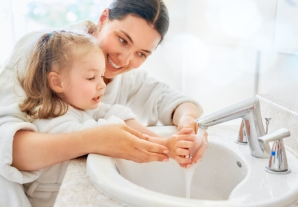 A woman gently washing the hands of a young girl at a sink