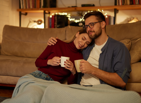 Woman and man sitting on the floor next to the couch with both of them holding a cup
